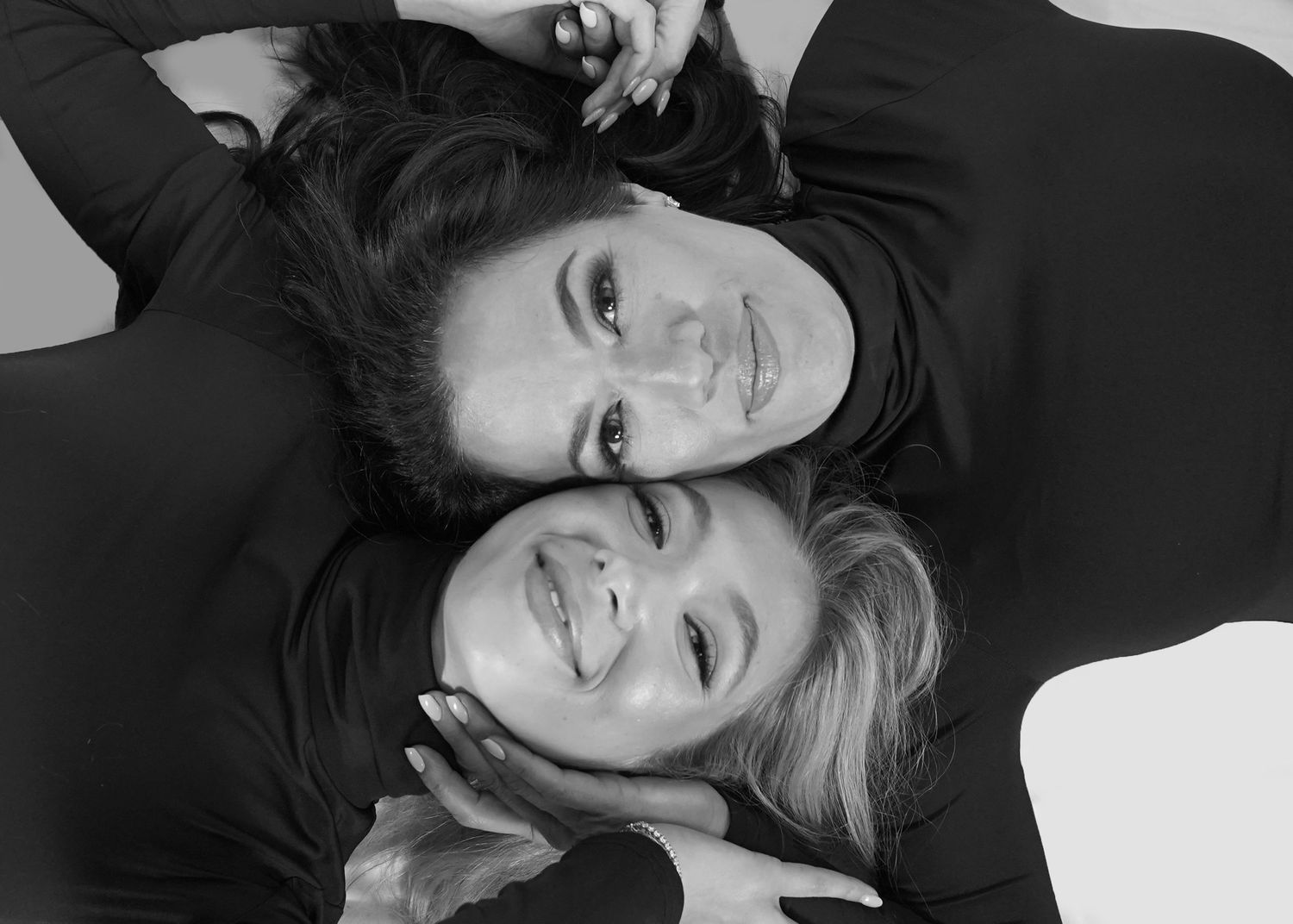 Black and white portrait of two people laying head to head in dark clothing.