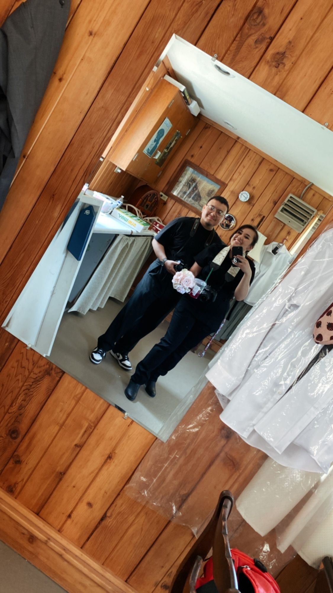 Three people pose for a mirror selfie in a wooden-paneled room.