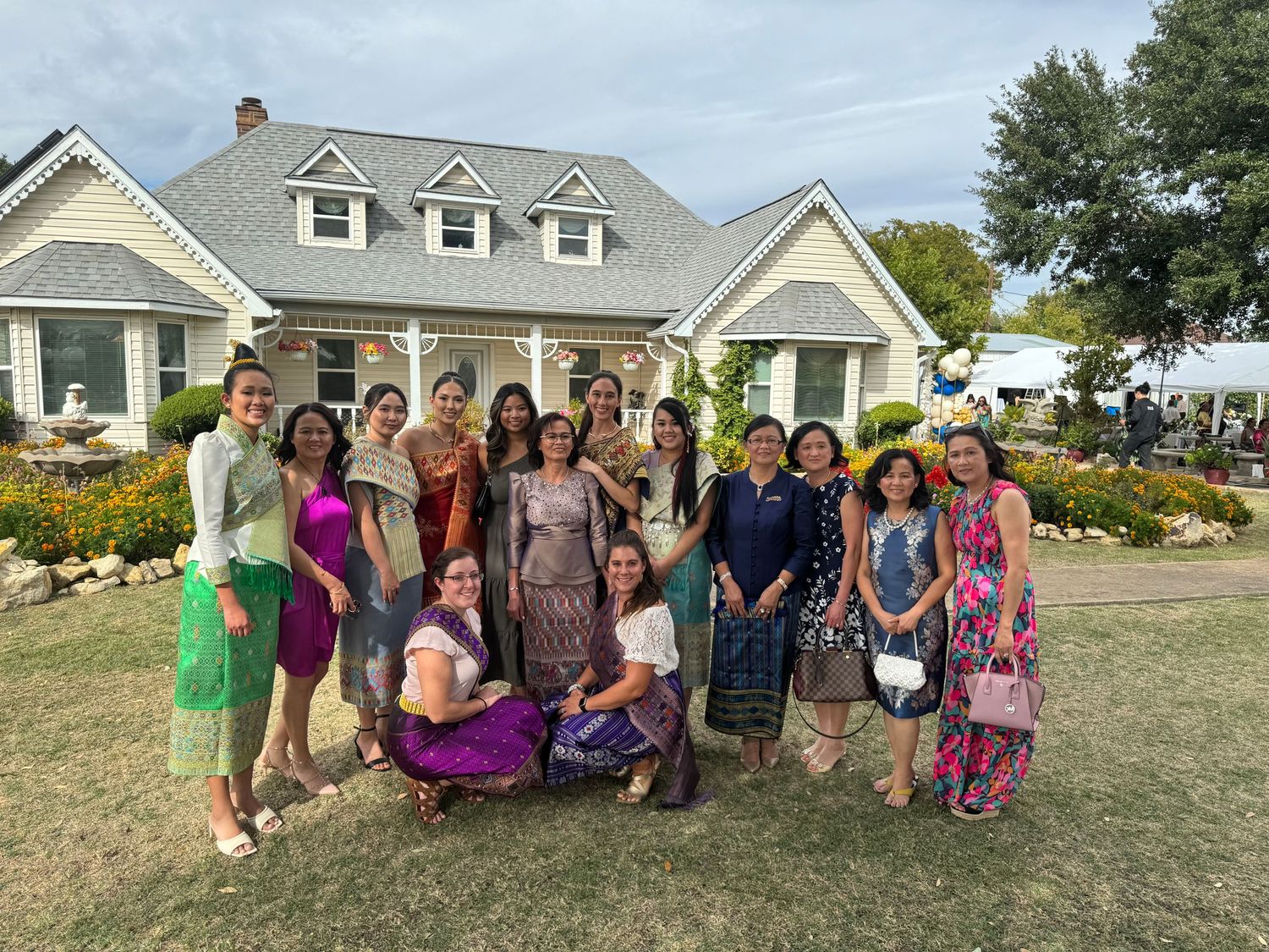 A group photo of people gathered outside a white Cape Cod style house with dormers.