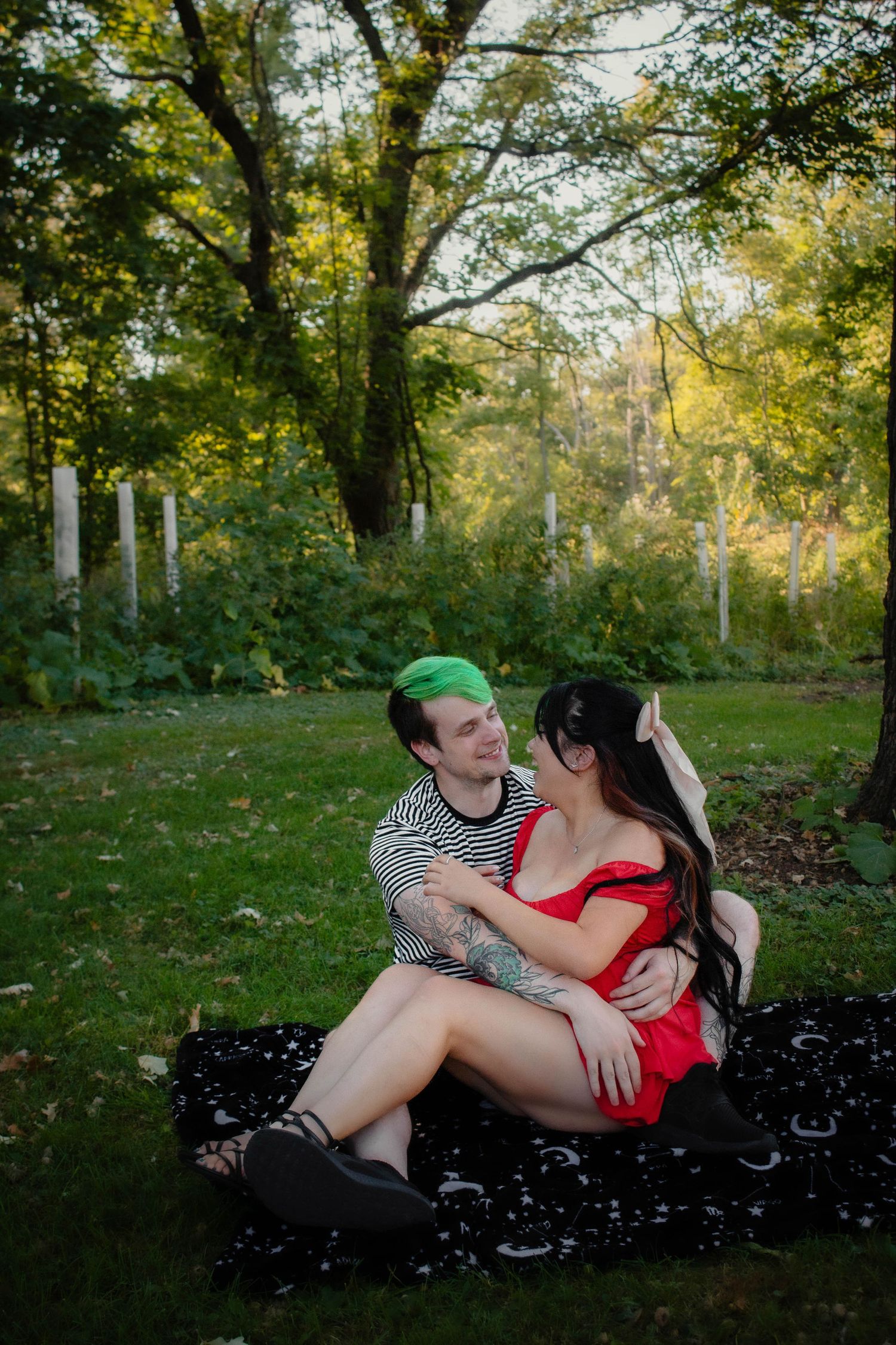 Couple shares intimate moment while relaxing on blanket in sunlit wooded area.