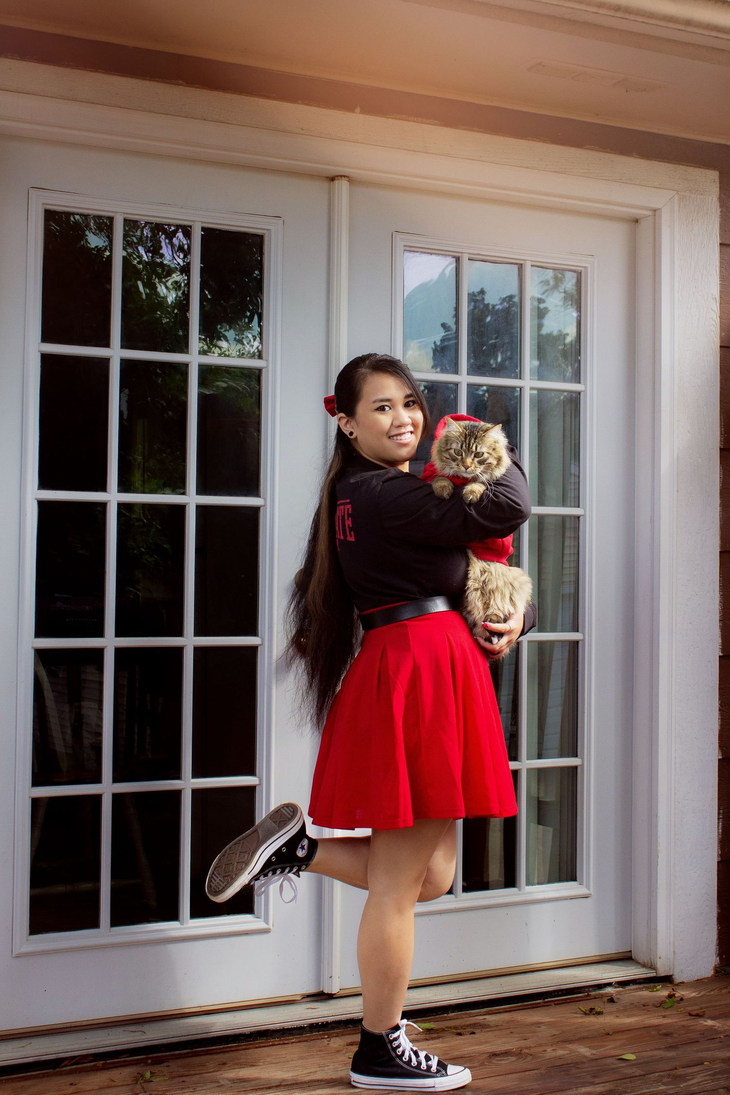 Someone in a red skirt and black top poses playfully against white French doors.
