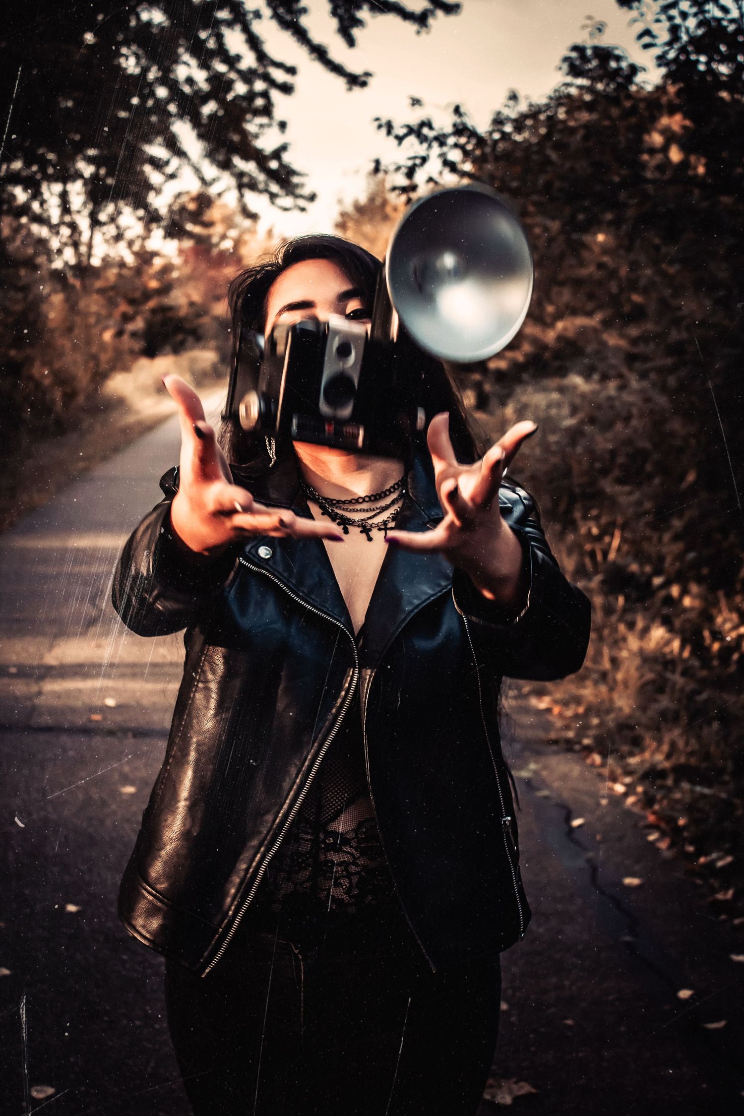 Person in leather jacket poses artistically with camera equipment at dusk.