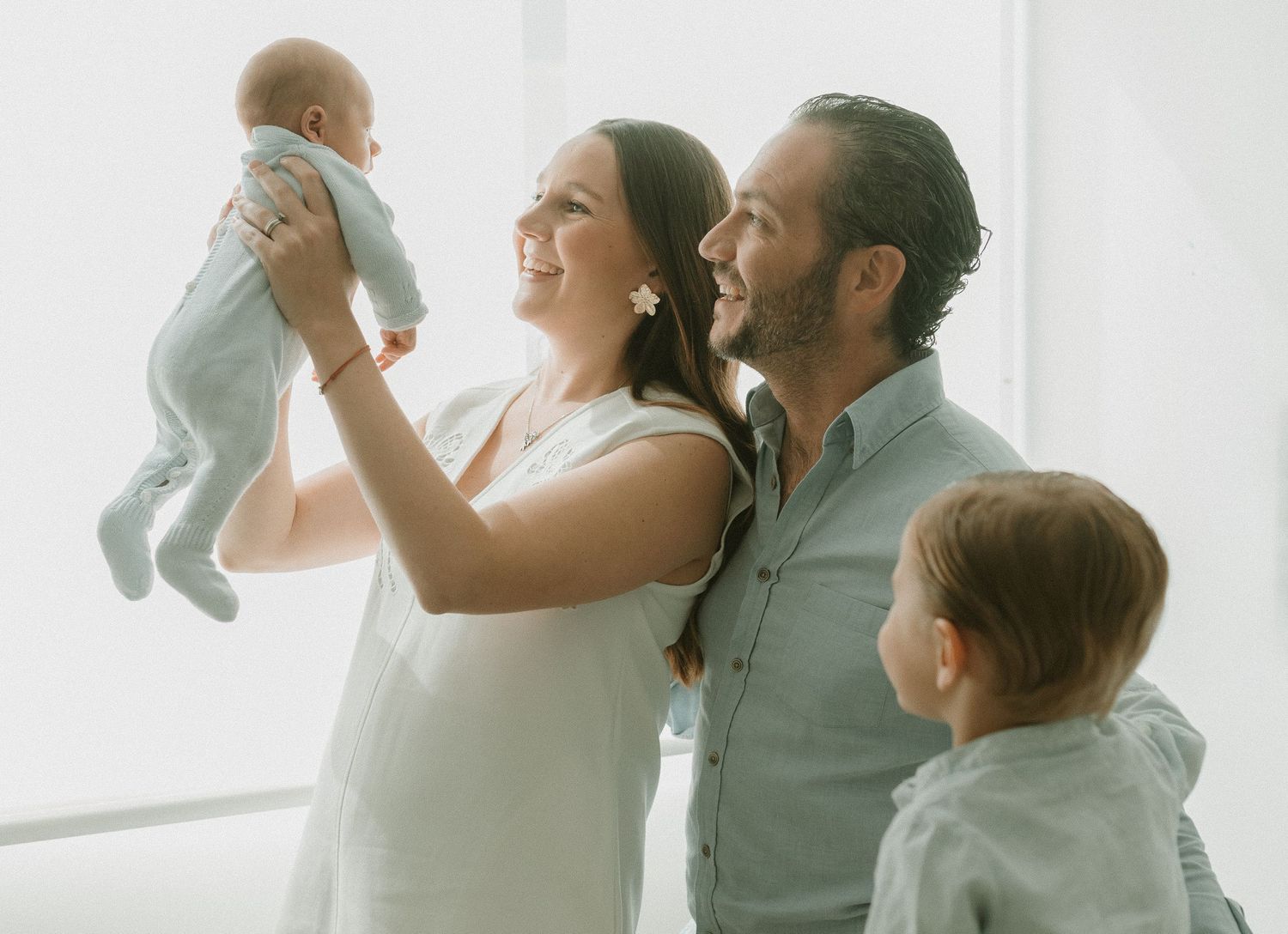 Joyful family moment as parents lift their baby while a toddler watches.