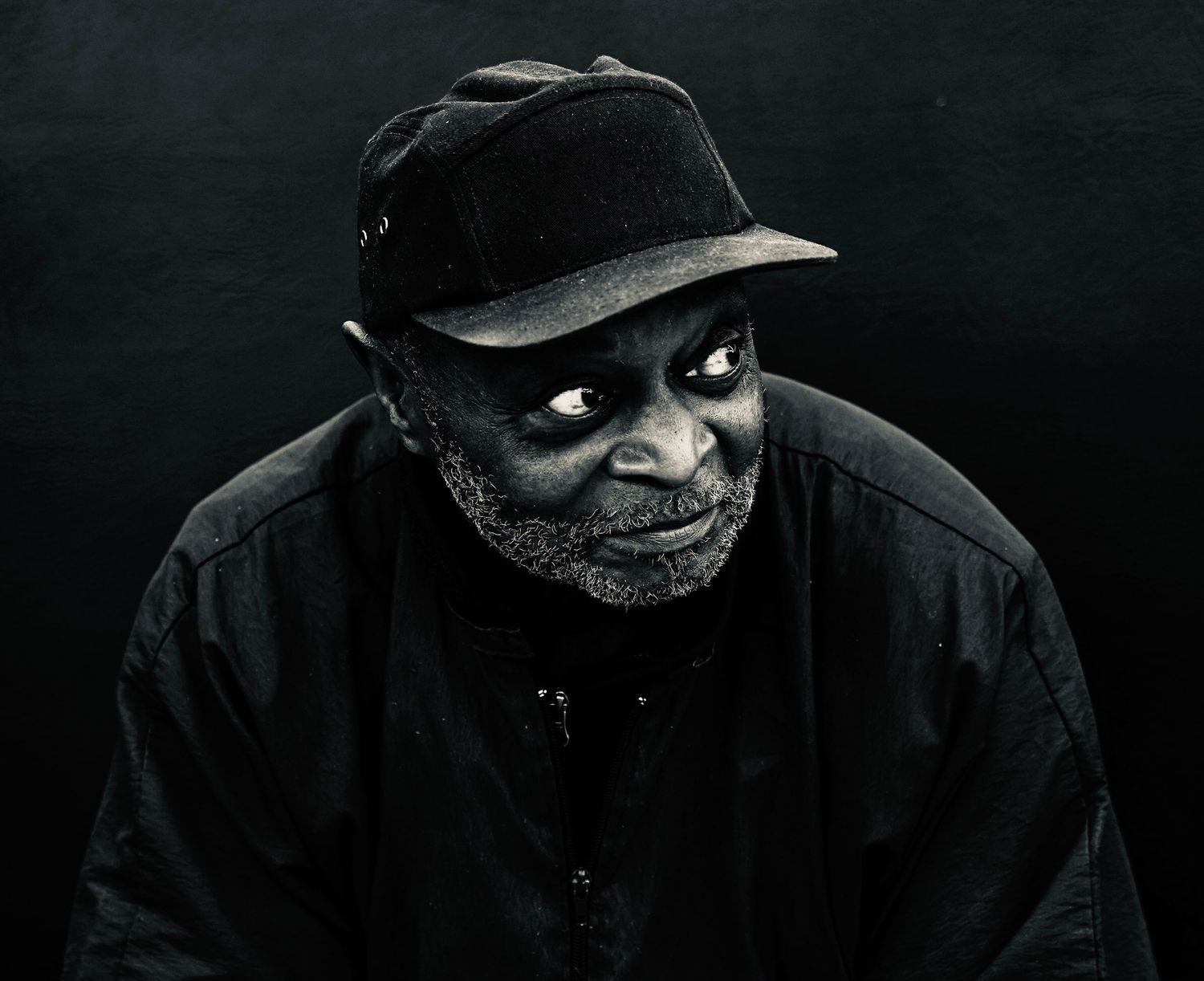 Portrait of a person wearing a black cap against dark background.