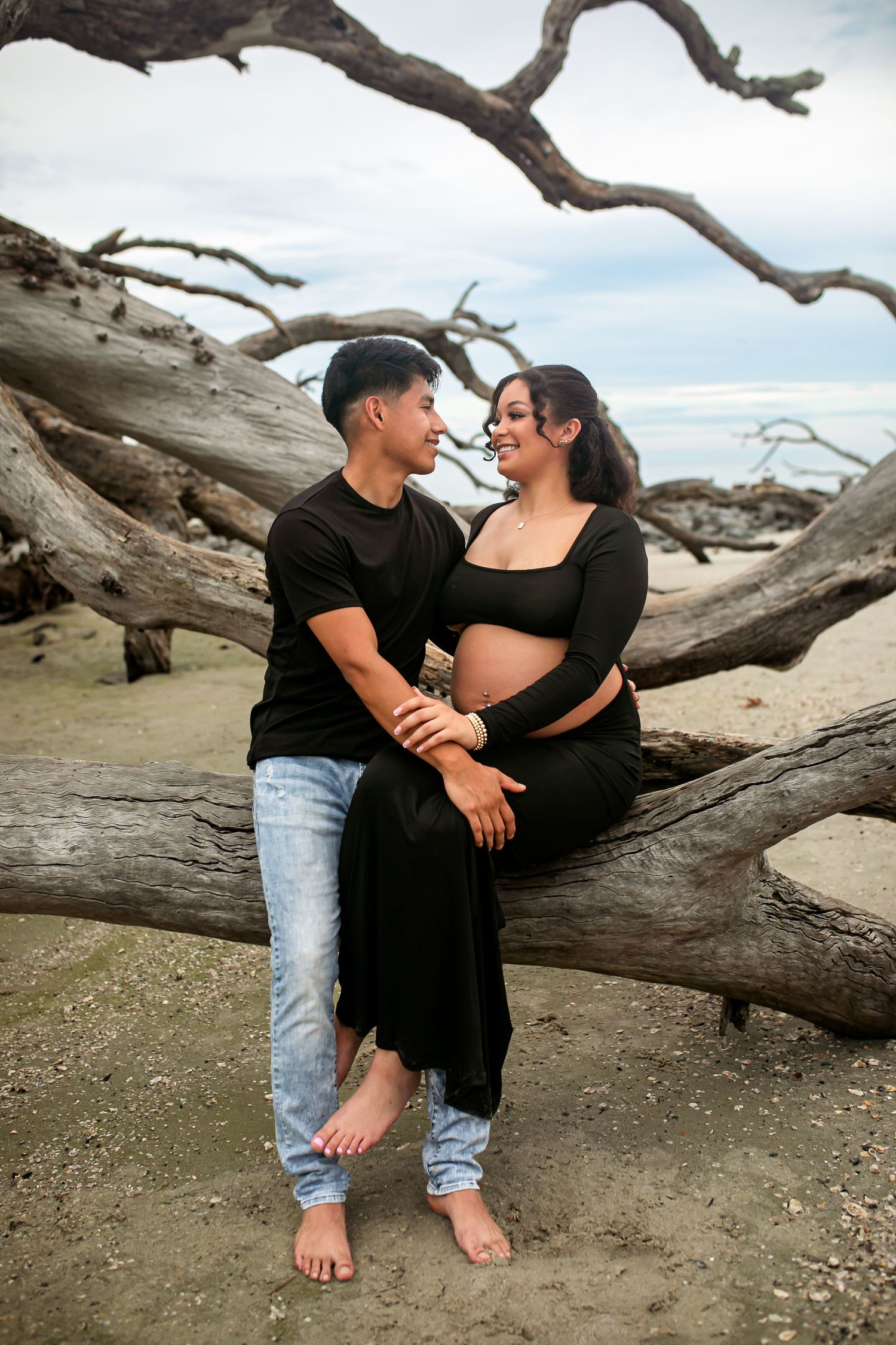 Black and white maternity photo with driftwood tree background on beach.