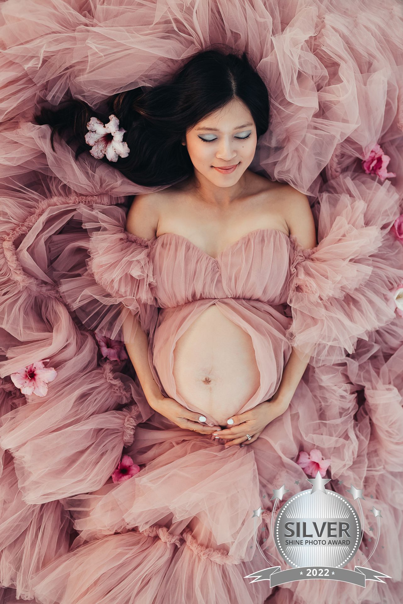 Maternity portrait in flowing pink tulle dress with floral accents.