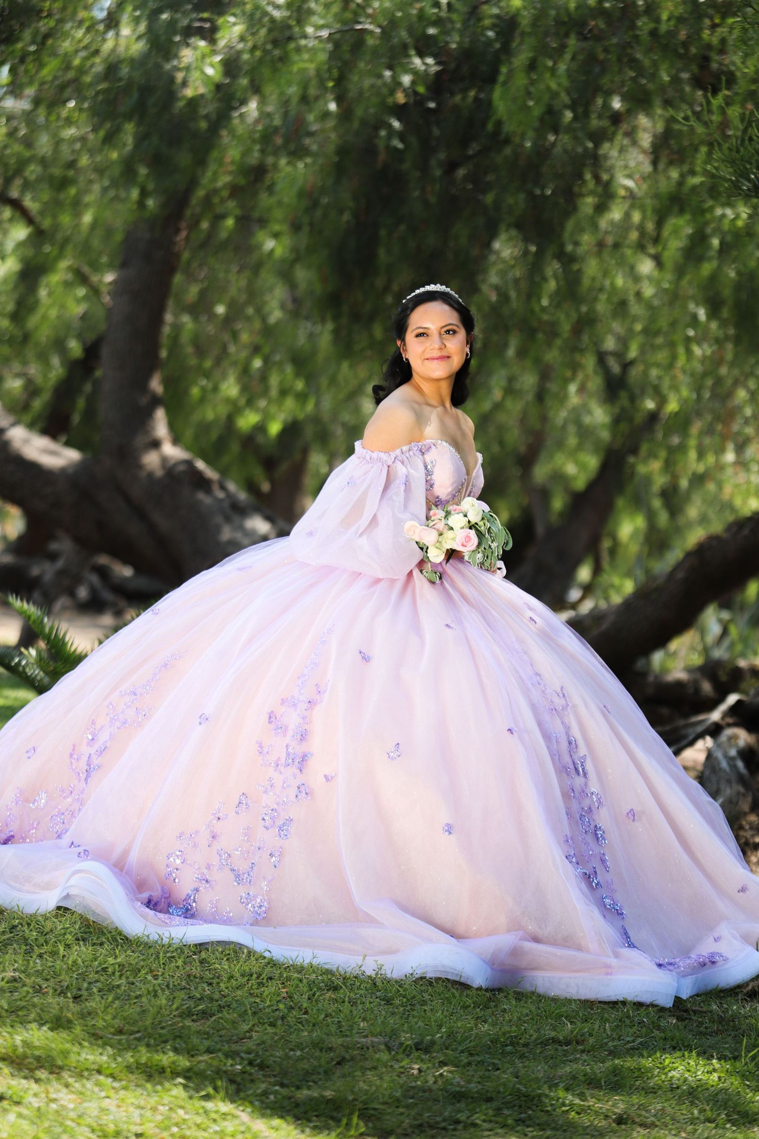 A lavender ballgown with delicate floral details photographed in a garden setting with weeping willow trees.