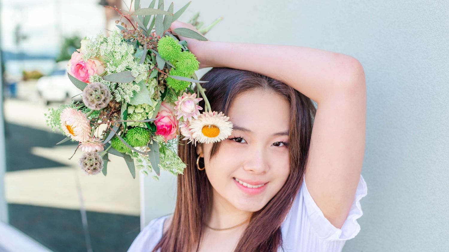 Person holding colorful floral bouquet with pink and white flowers against sunny backdrop.
