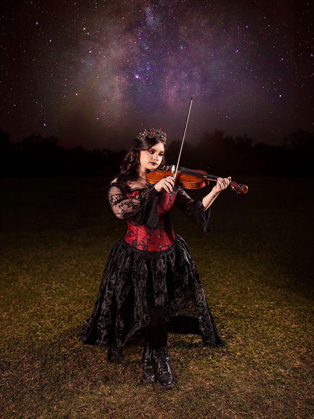 Gothic violinist in red corset and black skirt plays under a stunning Milky Way night sky.