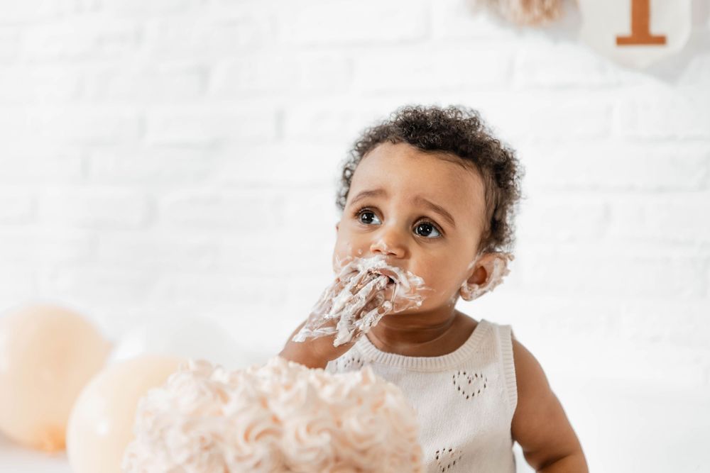 Adorable baby in white sweater smiles while sitting in elegant minimalist studio setup with soft lighting.