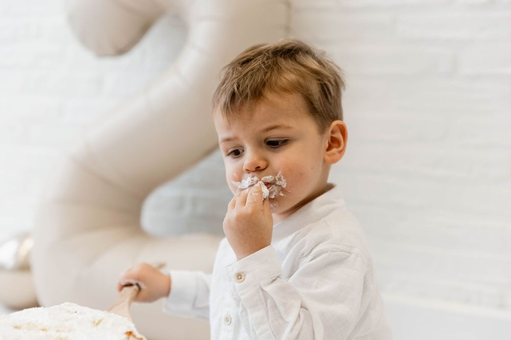 Young child in white shirt enjoys eating a snack while sitting indoors.