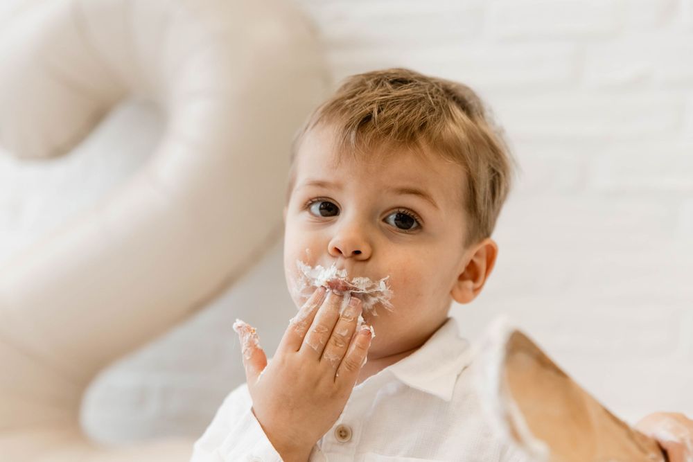 Two children with messy faces smile and play with whipped cream while making a fun mess at home.