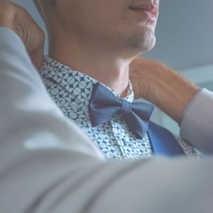 Préparatif du marié, quelqu'un lui remet son noeud papillon en place. Photographie de mariage, homme. Flashnoah photo