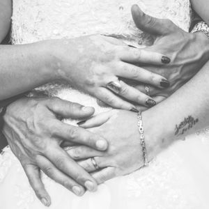 Gros plan des mains des marriés portant leurs alliances respectives, photo noir & blanc prise par Flashnoah