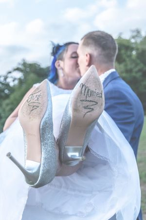 Gros plan mariage. Le marié porte son épouse, dont on vois les inscription "just married" sous ses chaussures à talons.