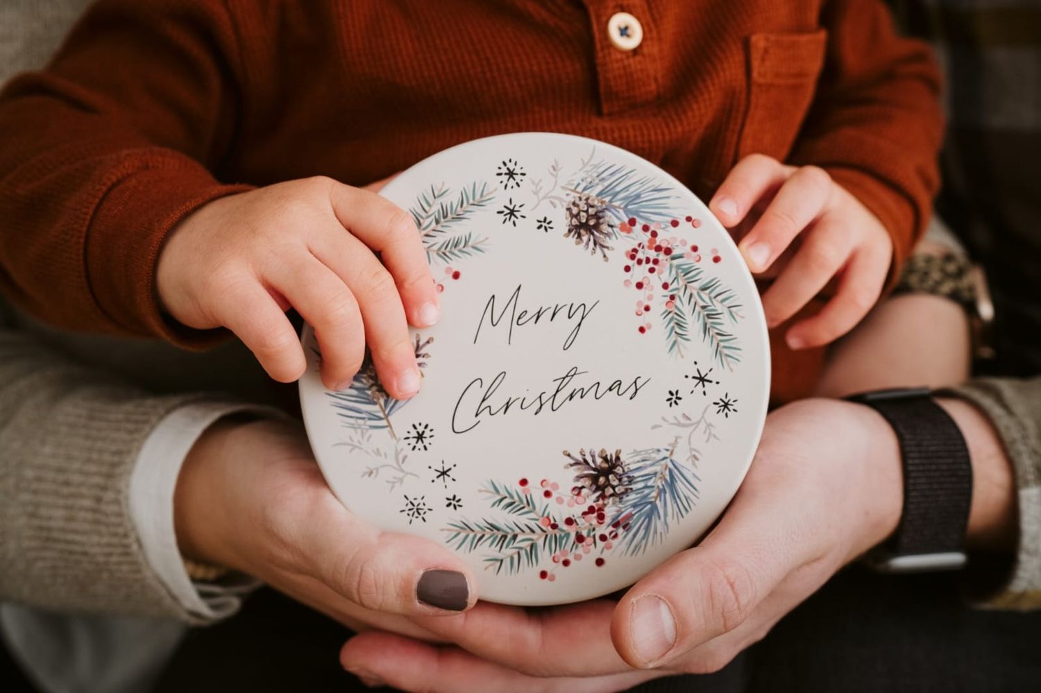 Hands holding decorative Christmas ornaments with festive messages.