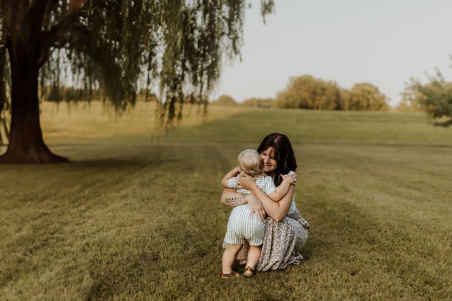 Natural maternity portraits on grassy hill during golden hour.
