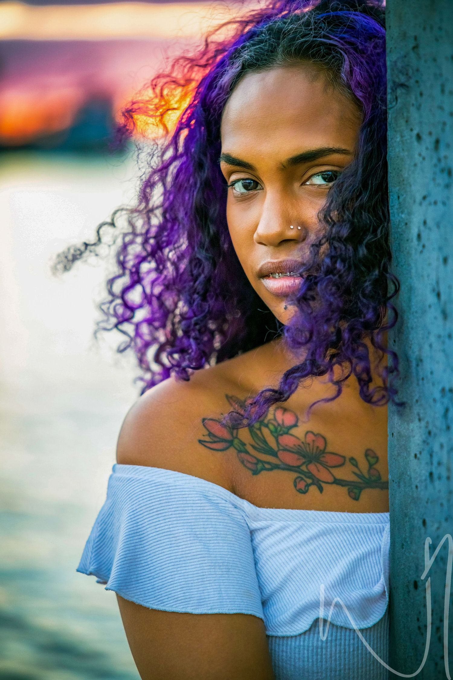 Sunset portrait with purple curly hair against blue water background.