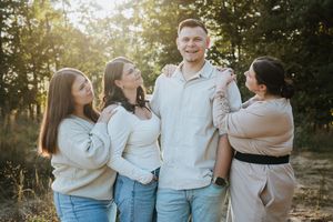 Family members embrace and laugh together during sunset photoshoot in casual attire.