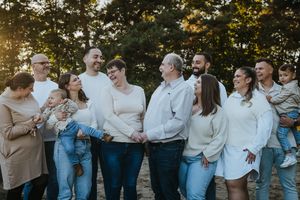 Large group poses casually in coordinated blue and cream outfits during outdoor photography session.