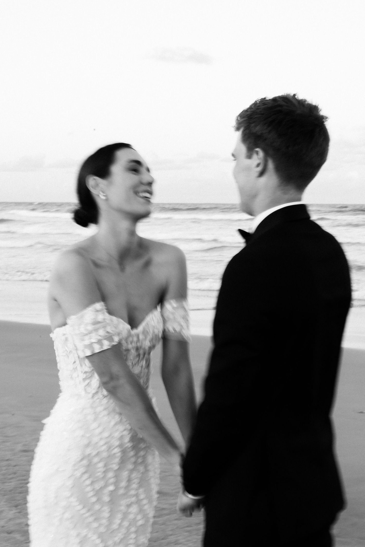 A romantic black and white beach wedding photo of a couple sharing a joyful moment by the ocean.