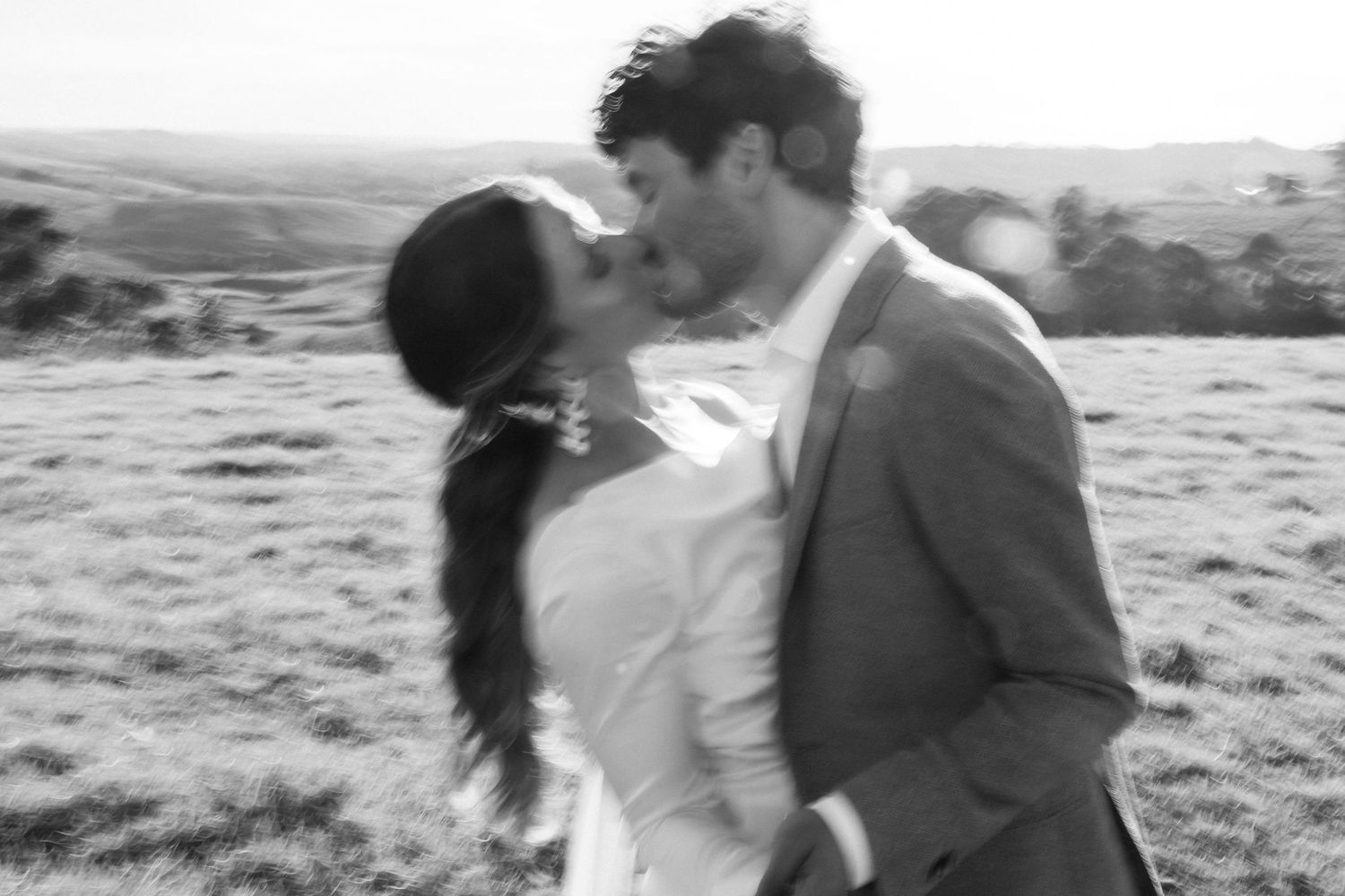 A dreamy black and white wedding photo capturing a romantic moment in a scenic hillside setting.