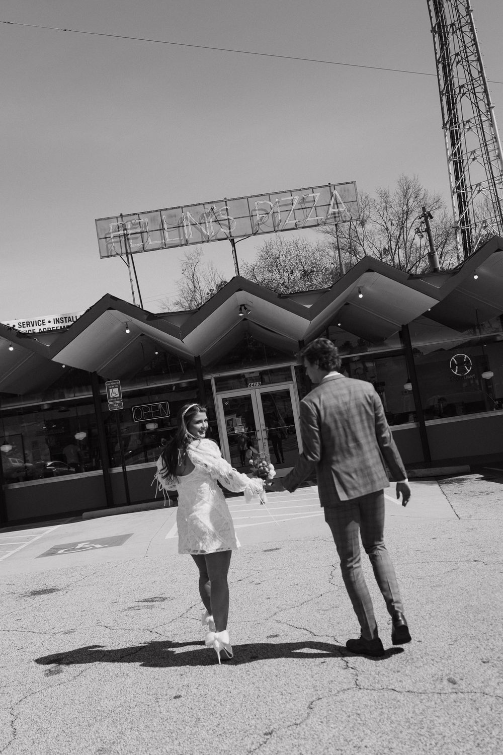 Black and white photo of newlyweds holding hands outside a pizza restaurant after their wedding.