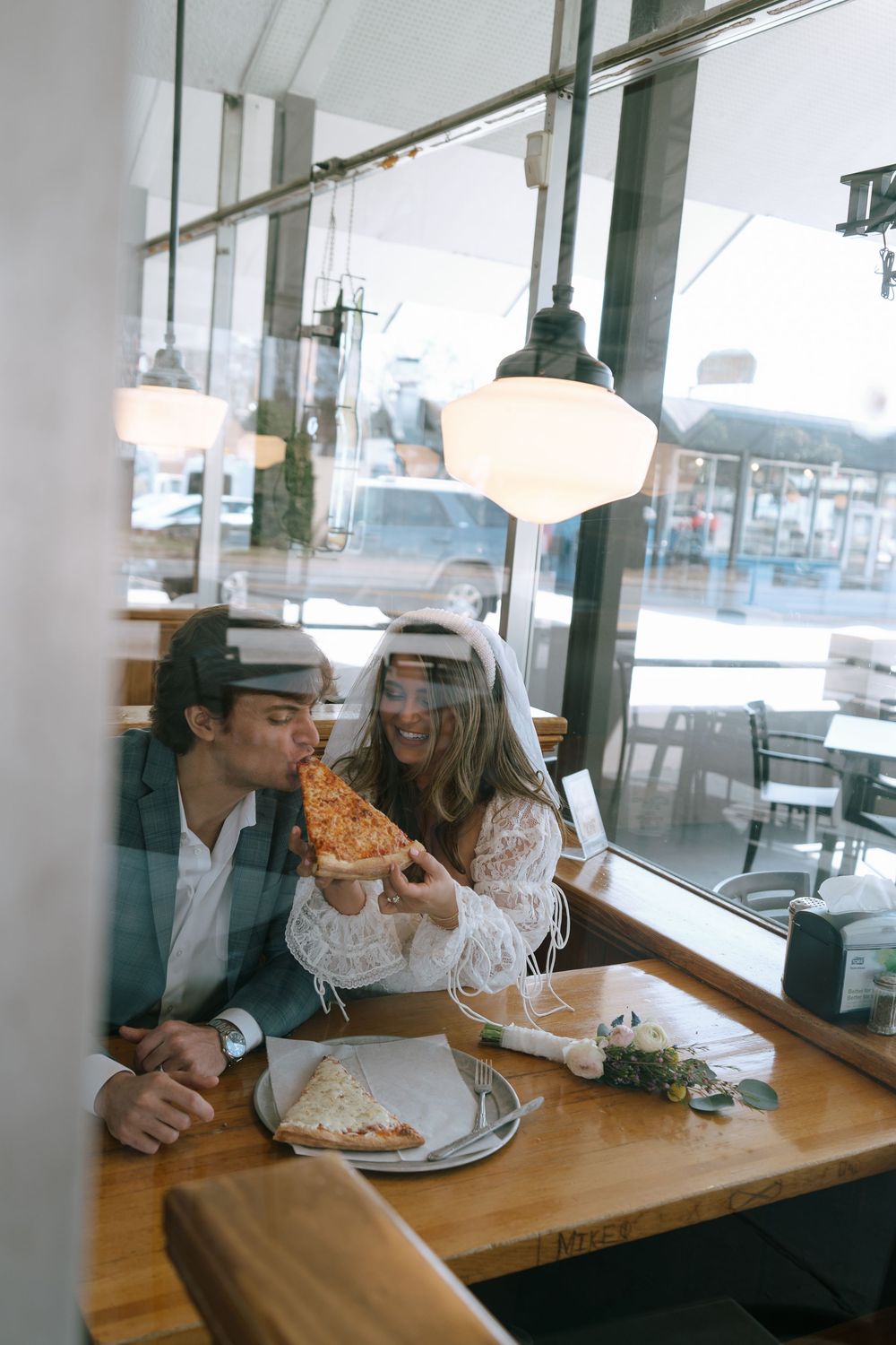 Newlyweds sharing a slice of pizza together inside a restaurant on their wedding day.