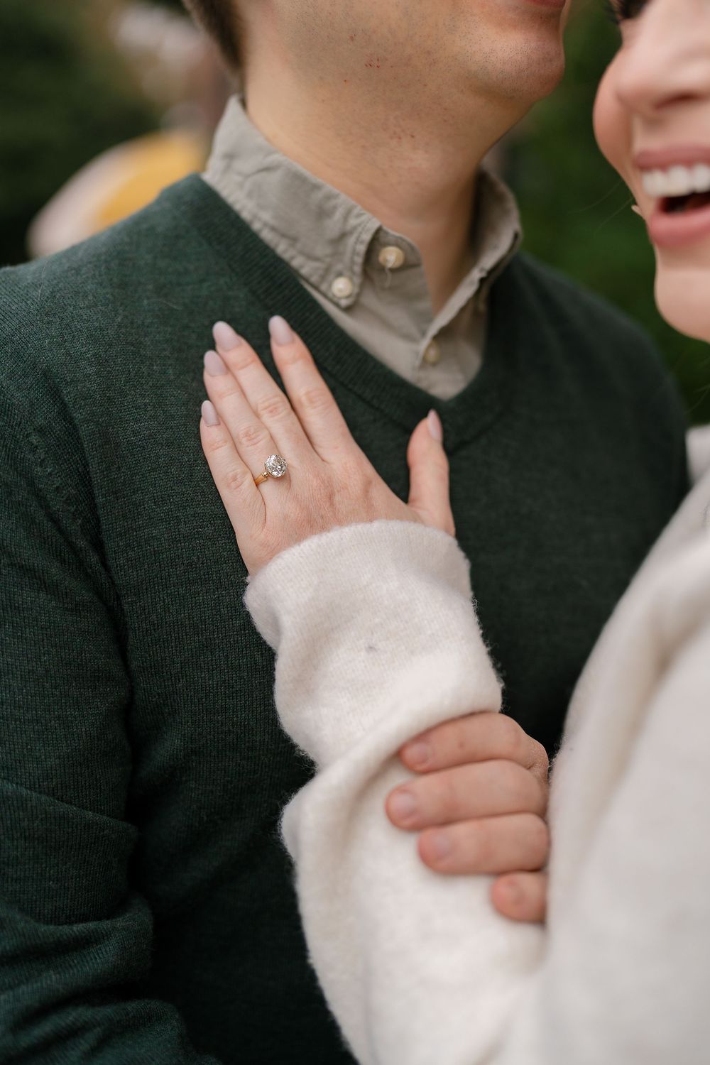 Close-up of woman's hand with diamond engagement ring resting on man's green sweater.