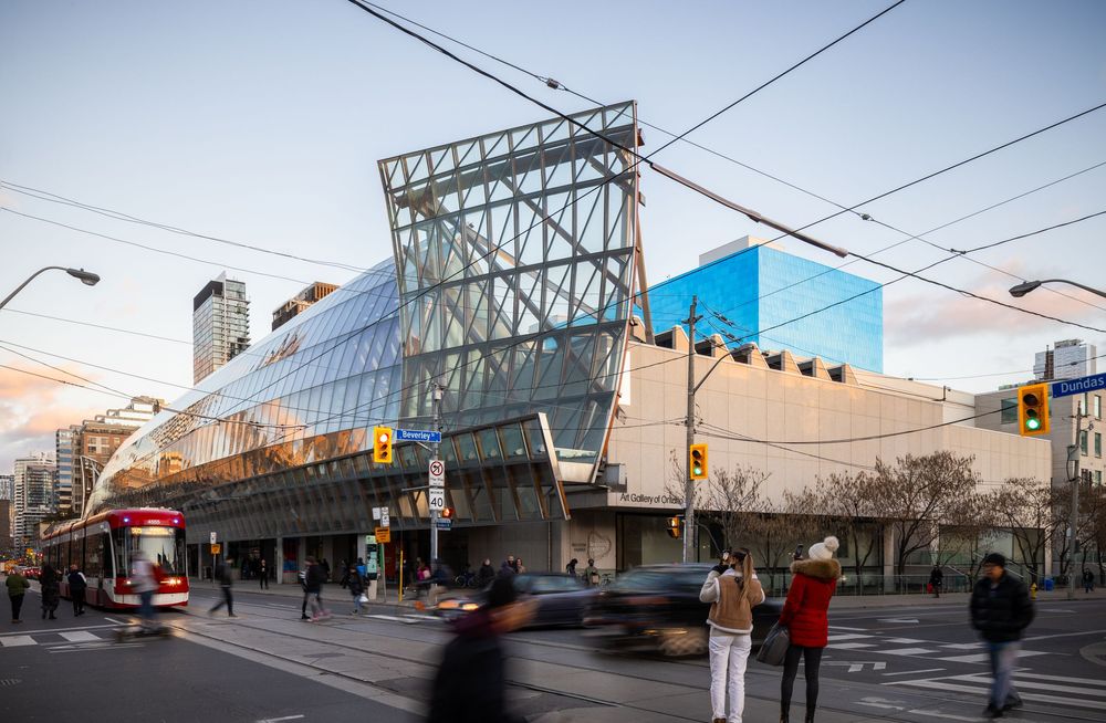Modern glass and steel building at a busy Toronto intersection with streetcar and pedestrians at dusk.