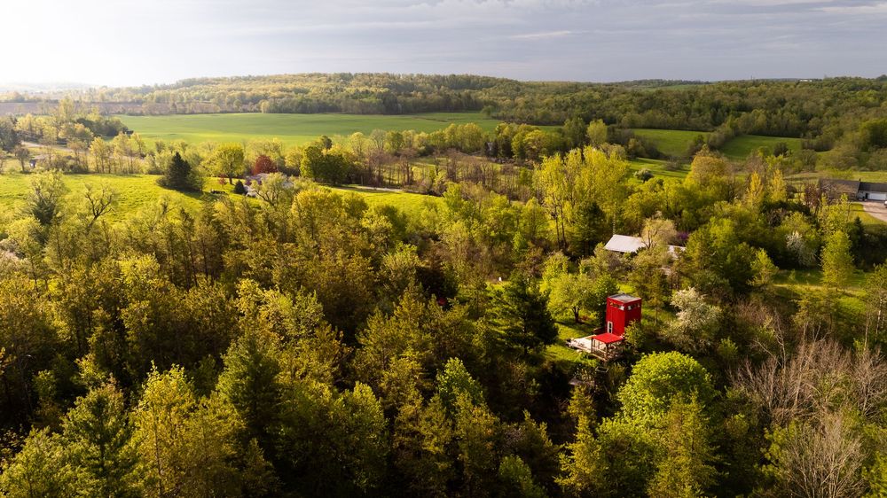 Aerial view of lush green countryside with a red barn nestled among trees under a partly cloudy sky.