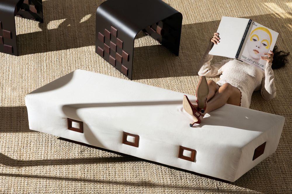 Woman relaxing on a white sculptural chaise lounge reading a book, with a dark geometric side table nearby.
