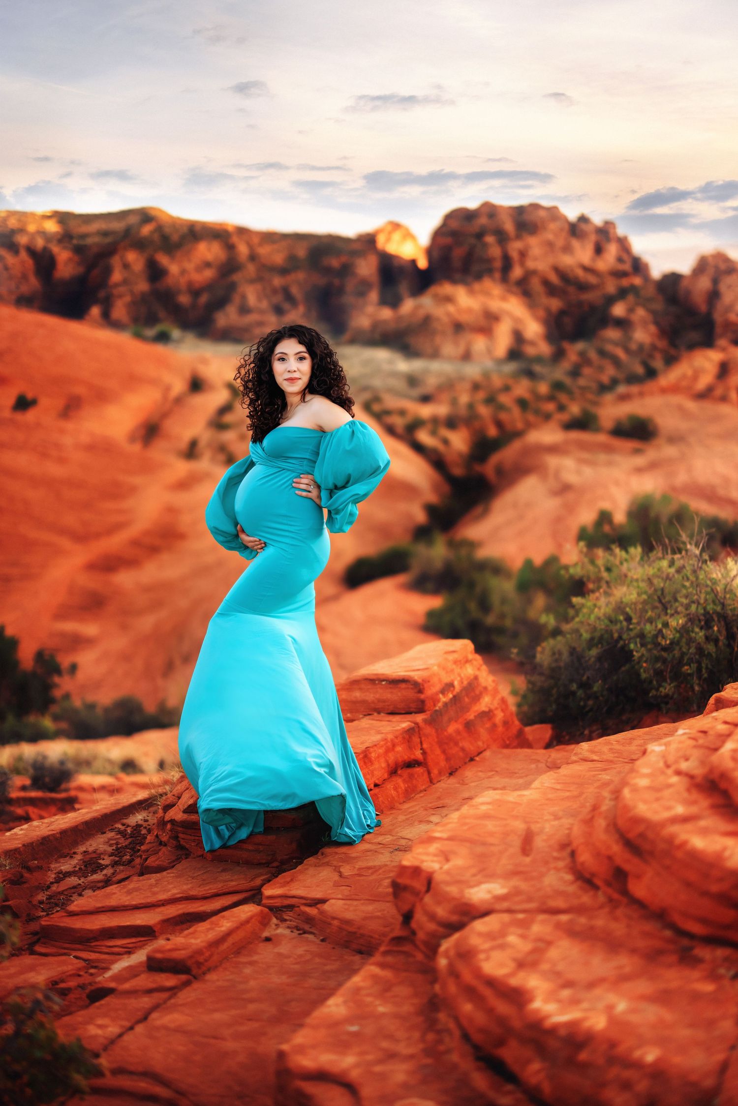 Person in turquoise dress poses on red rock formation during sunset in Snow Canyon State Park Utah