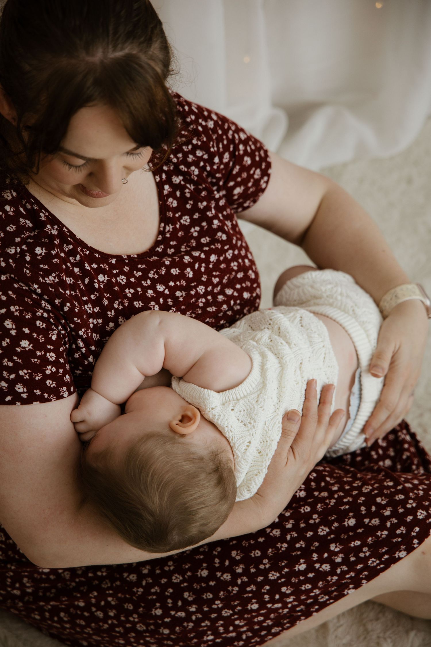 Newborn baby hand resting on parent's hand wearing a wedding ring against white clothing.