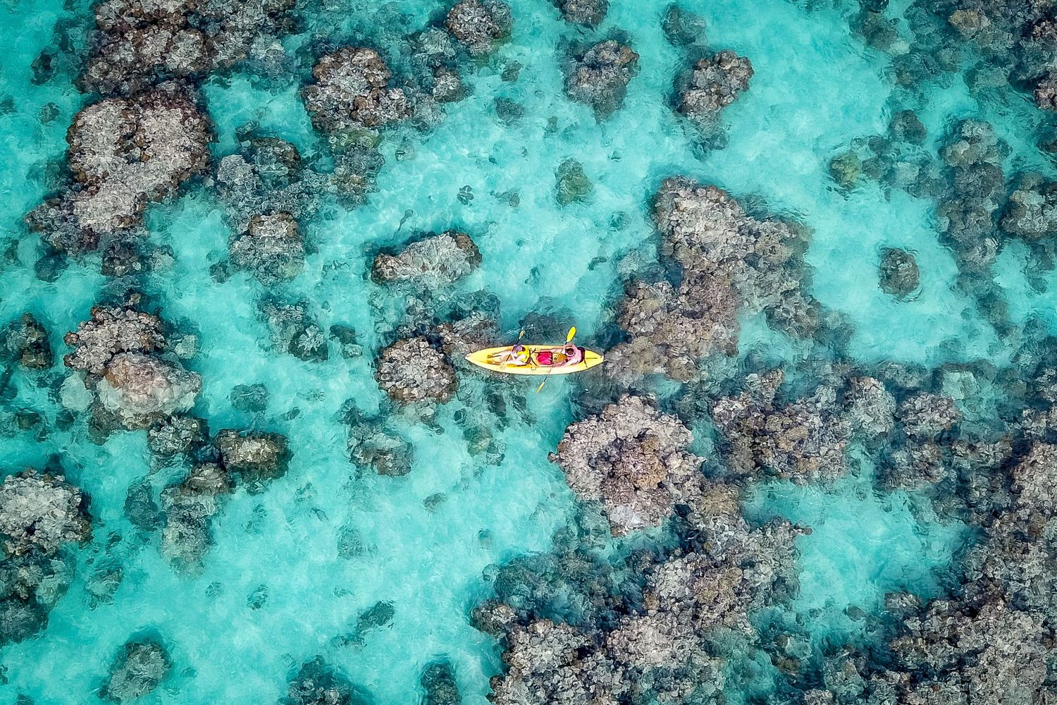Hawaii drone photography of a yellow kayak paddling over the turquoise ocean water and coral reefs of Lanikai.