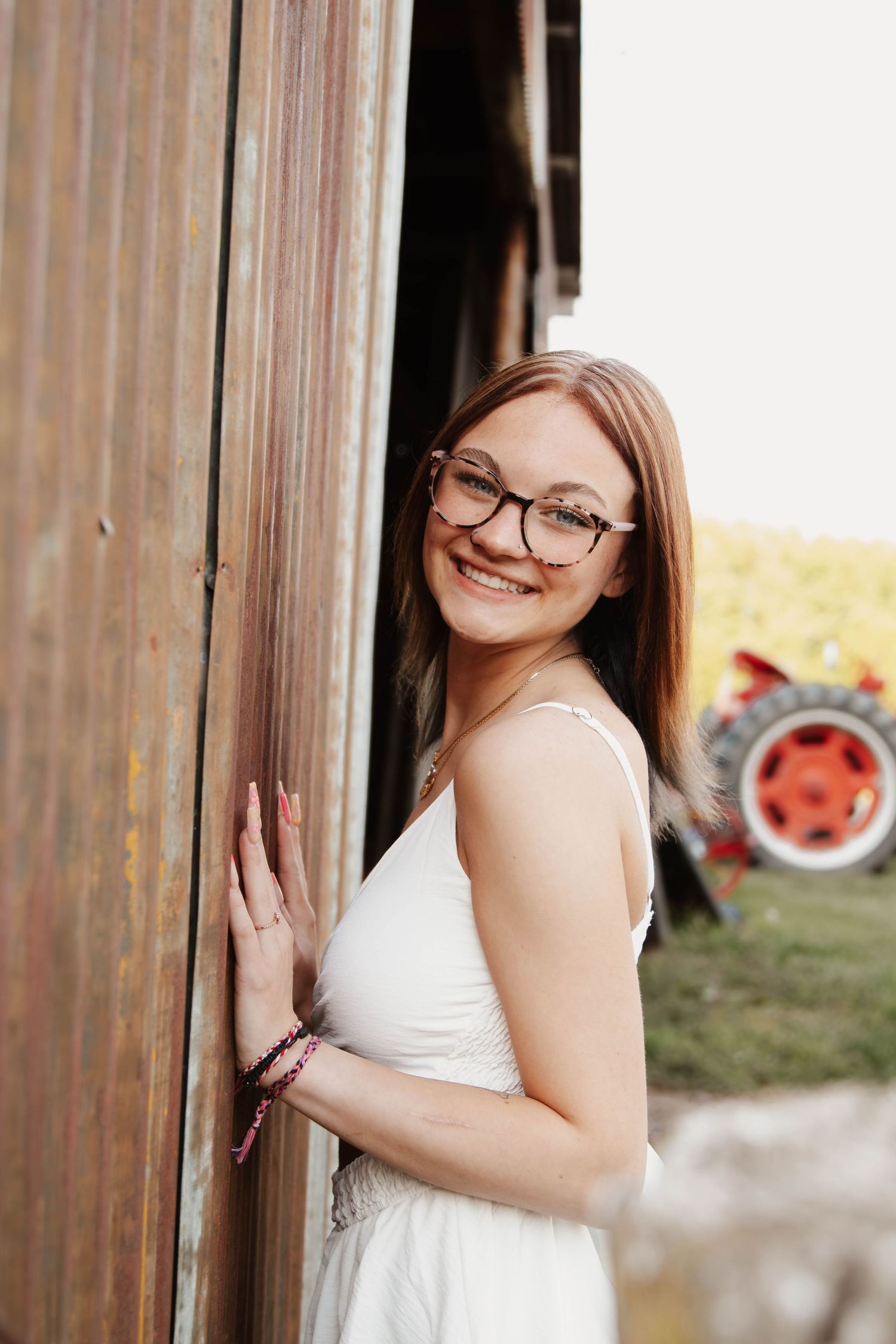 Portrait high school senior against rustic barn door with vintage tractor in background.