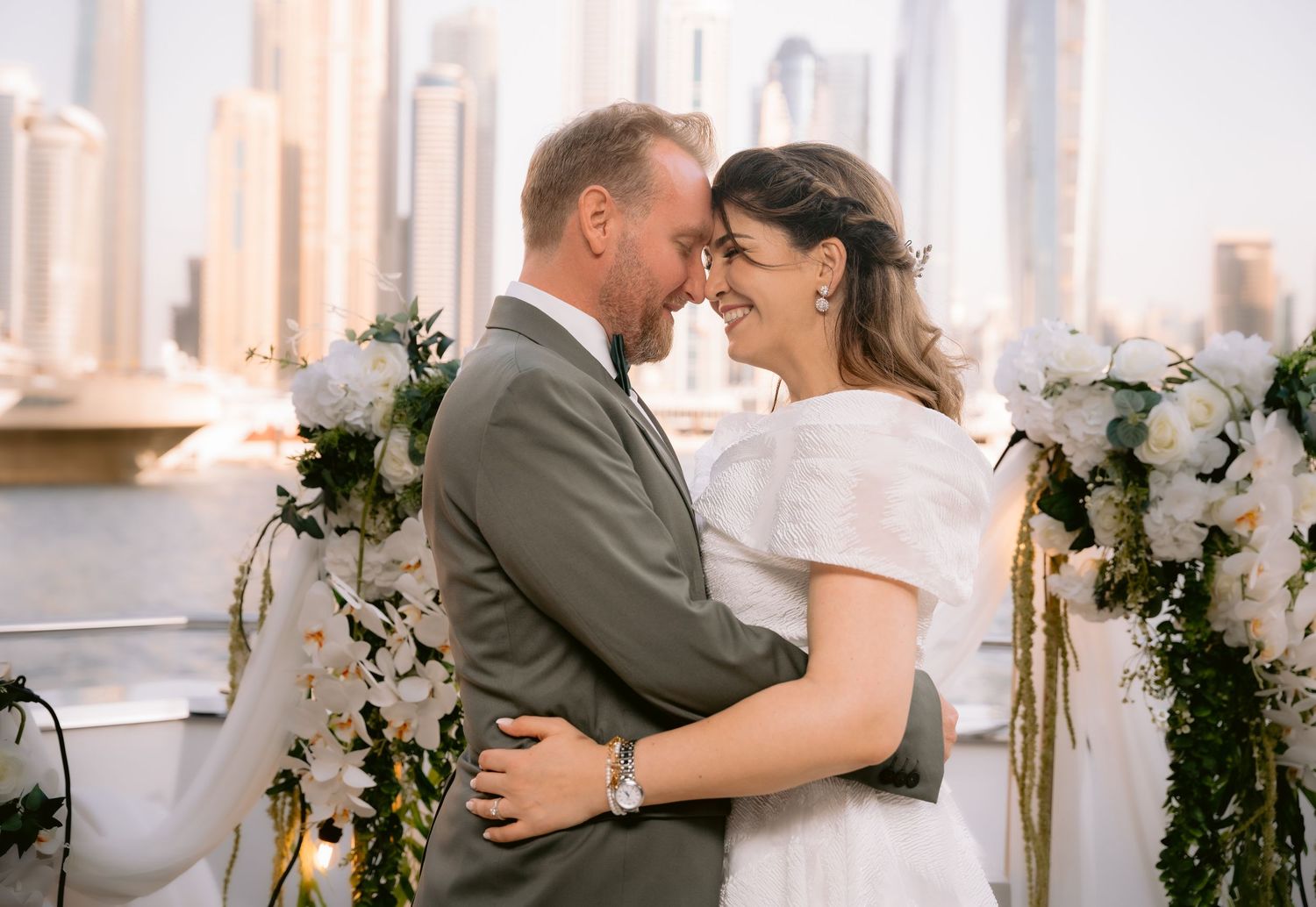 A couple in formalwear shares a tender moment during their wedding celebration in a bright white venue.