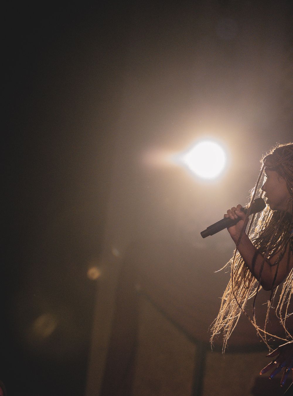 Silhouette of performer singing into microphone with bright backlighting creating atmospheric stage effect.