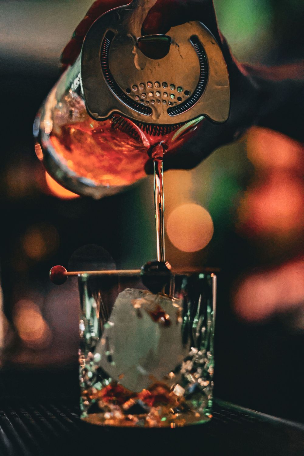 Close-up of red cocktail being poured through strainer into crystal glass.
