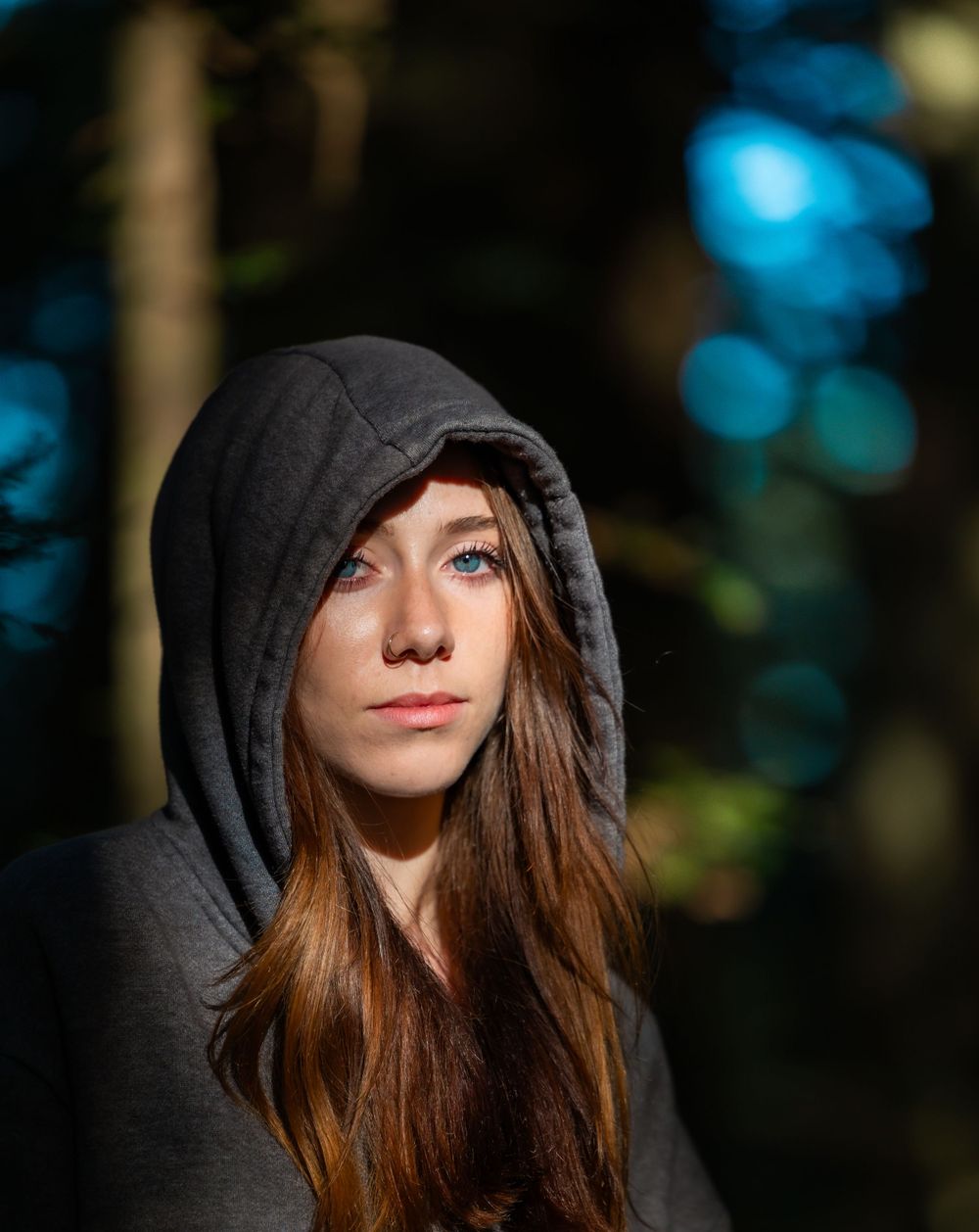 Person in black hoodie with long hair against blurred forest background.