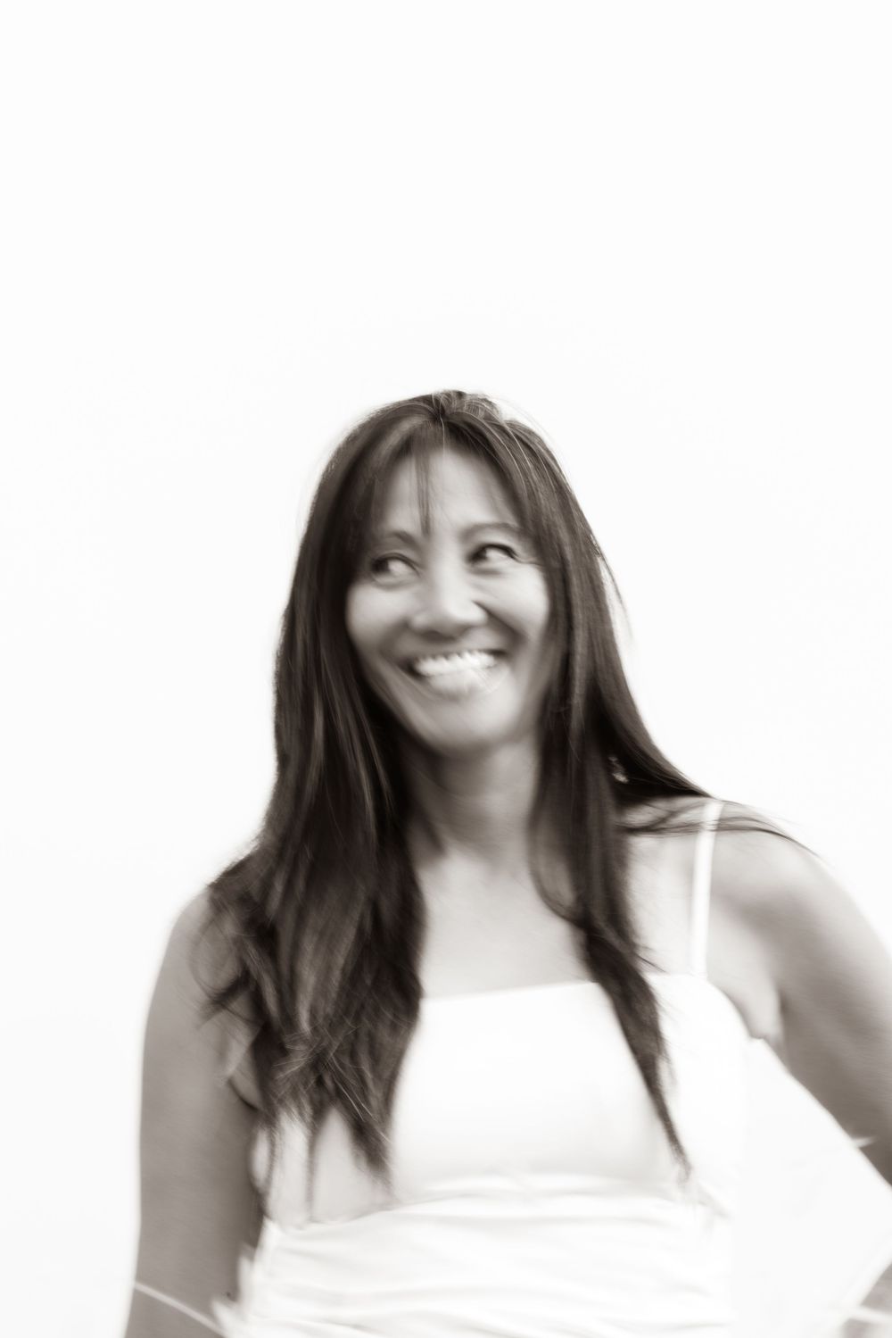 Smiling woman with long dark hair wearing a white top, black and white portrait photo.