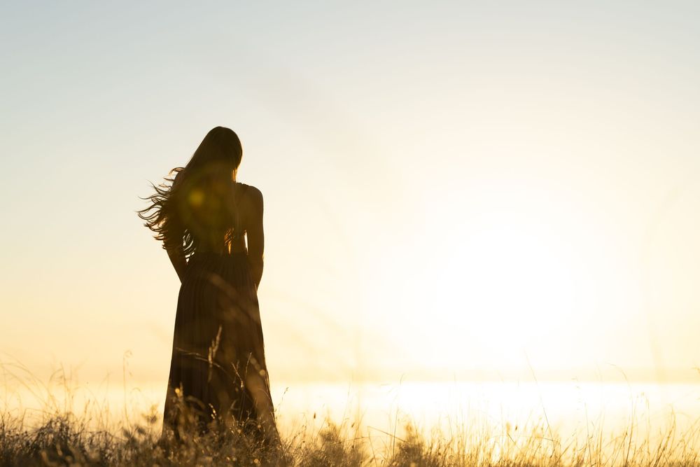Silhouetted figures stand in a golden field during sunset creating a dreamy atmospheric scene.