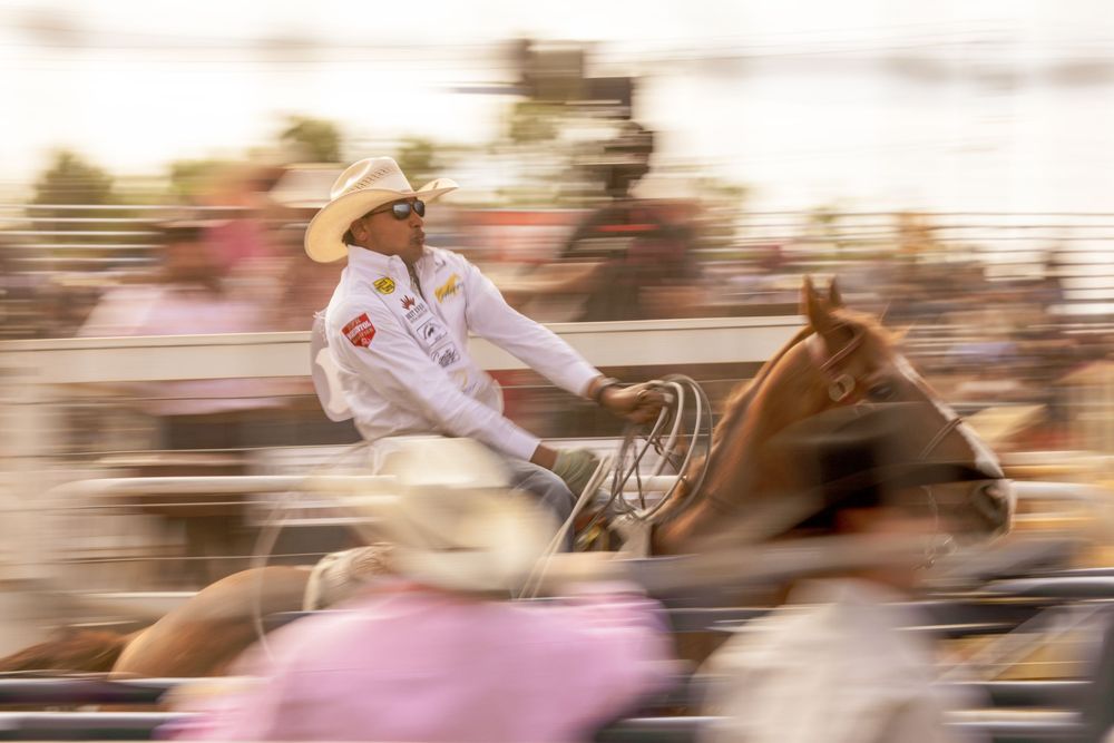 A cowboy in a white hat rides a horse at full speed during a rodeo event, captured with motion blur effect.