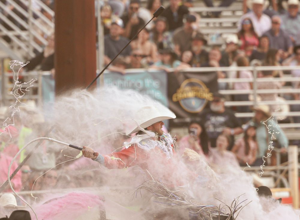 Rodeo clown in white fluffy costume performing at a crowded rodeo arena with spectators in the background.