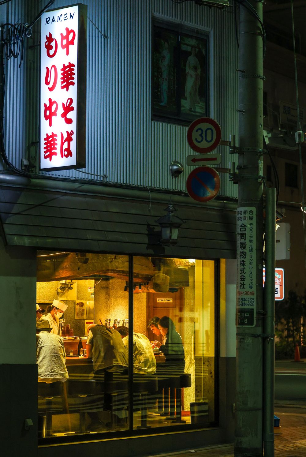 Glowing ramen restaurant at night in Japan with customers dining inside and illuminated Japanese signs outside.