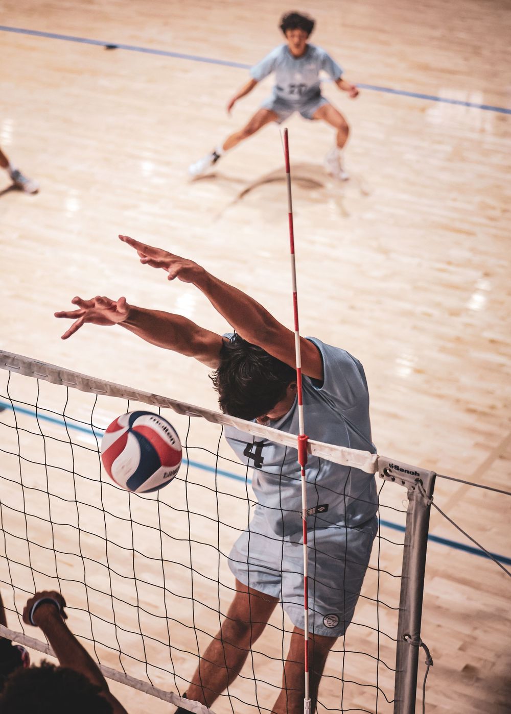 A sequence of volleyball players performing a powerful spike attack at the net during an indoor match.