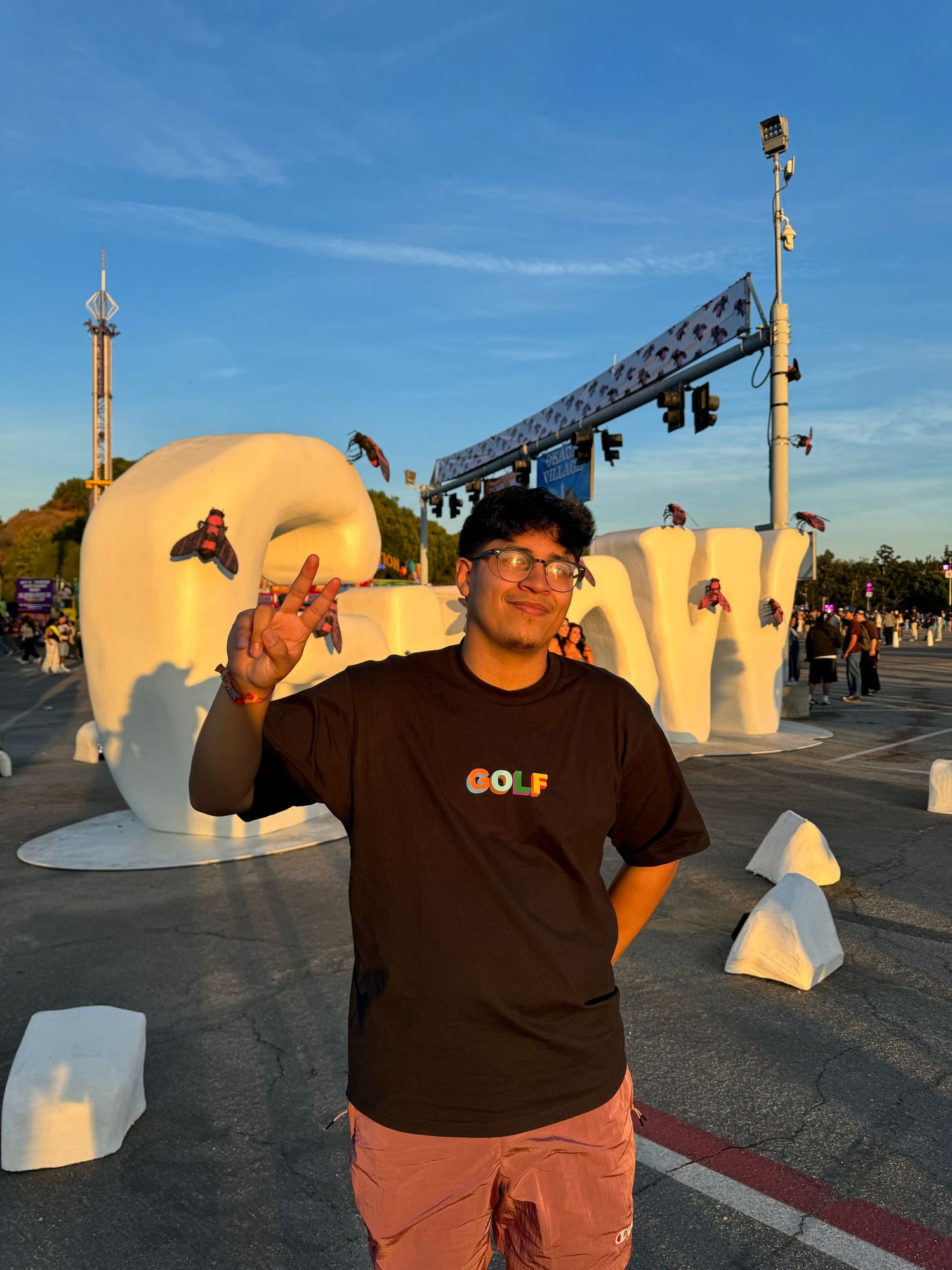 Person poses in front of white decorative outdoor installation wearing black top and brown pants during sunset.