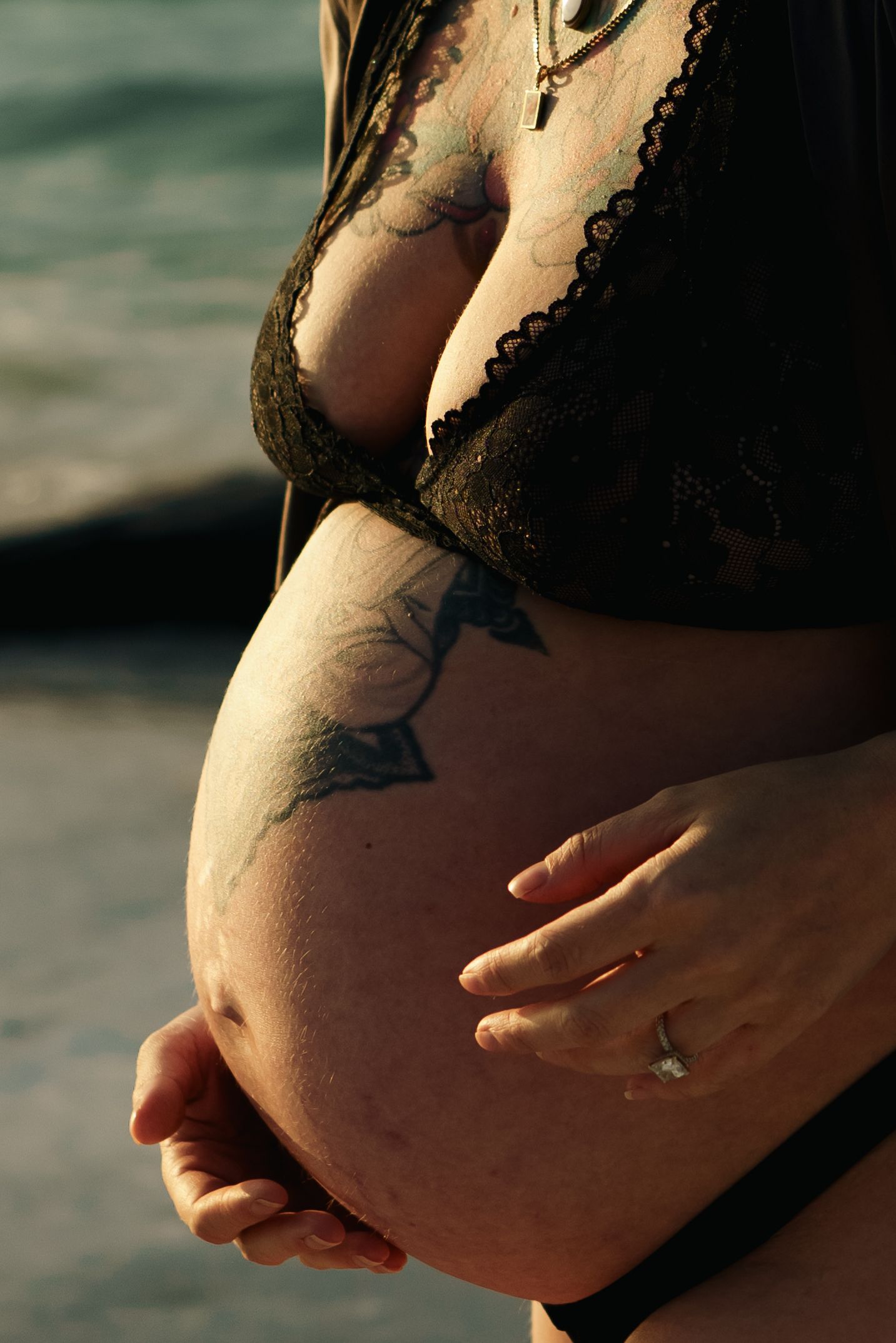 A tattooed pregnant belly photographed in natural light against a blurred background.