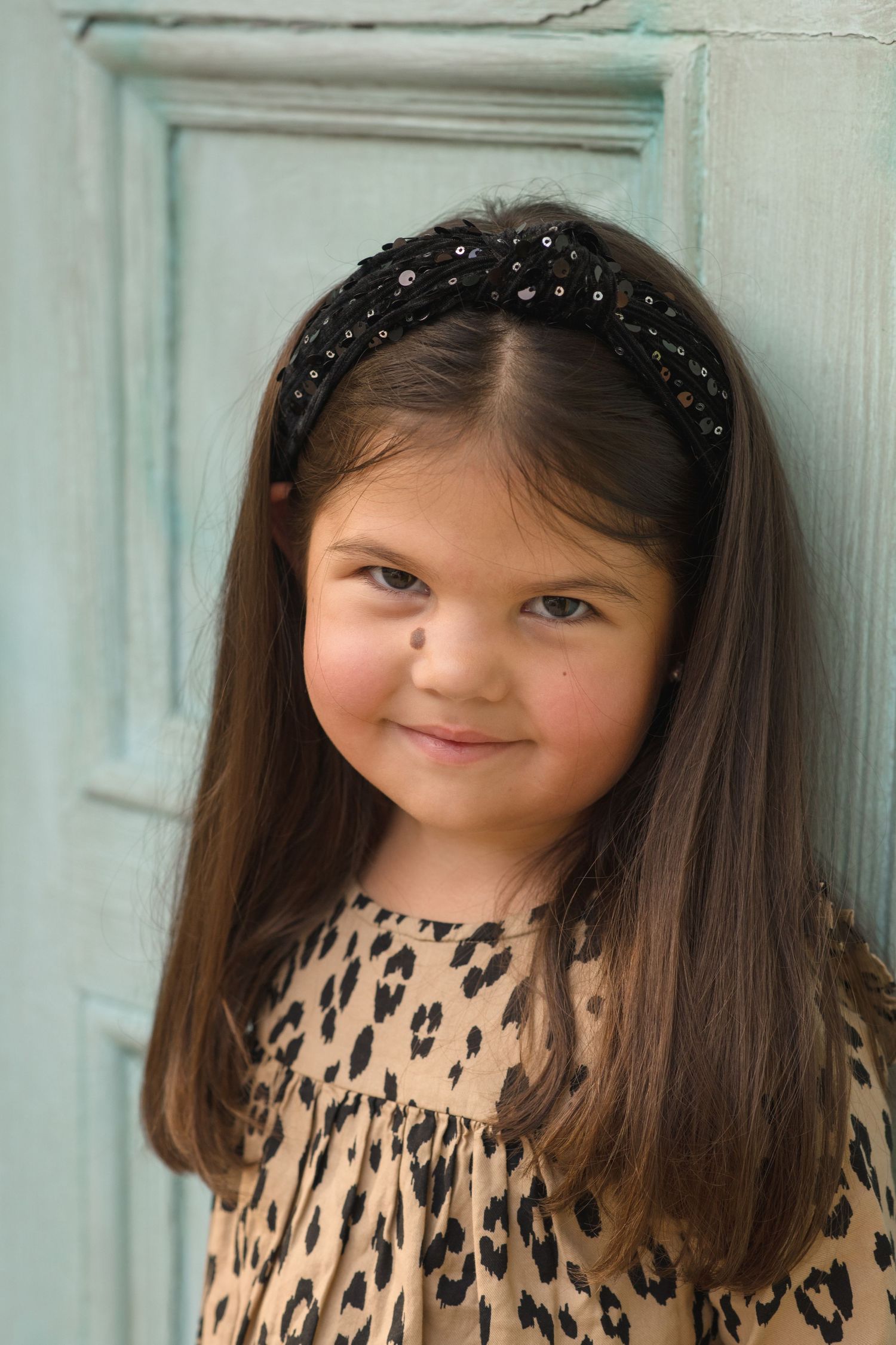 Young girl wearing a leopard print dress and hairband posing against a blue backdrop.