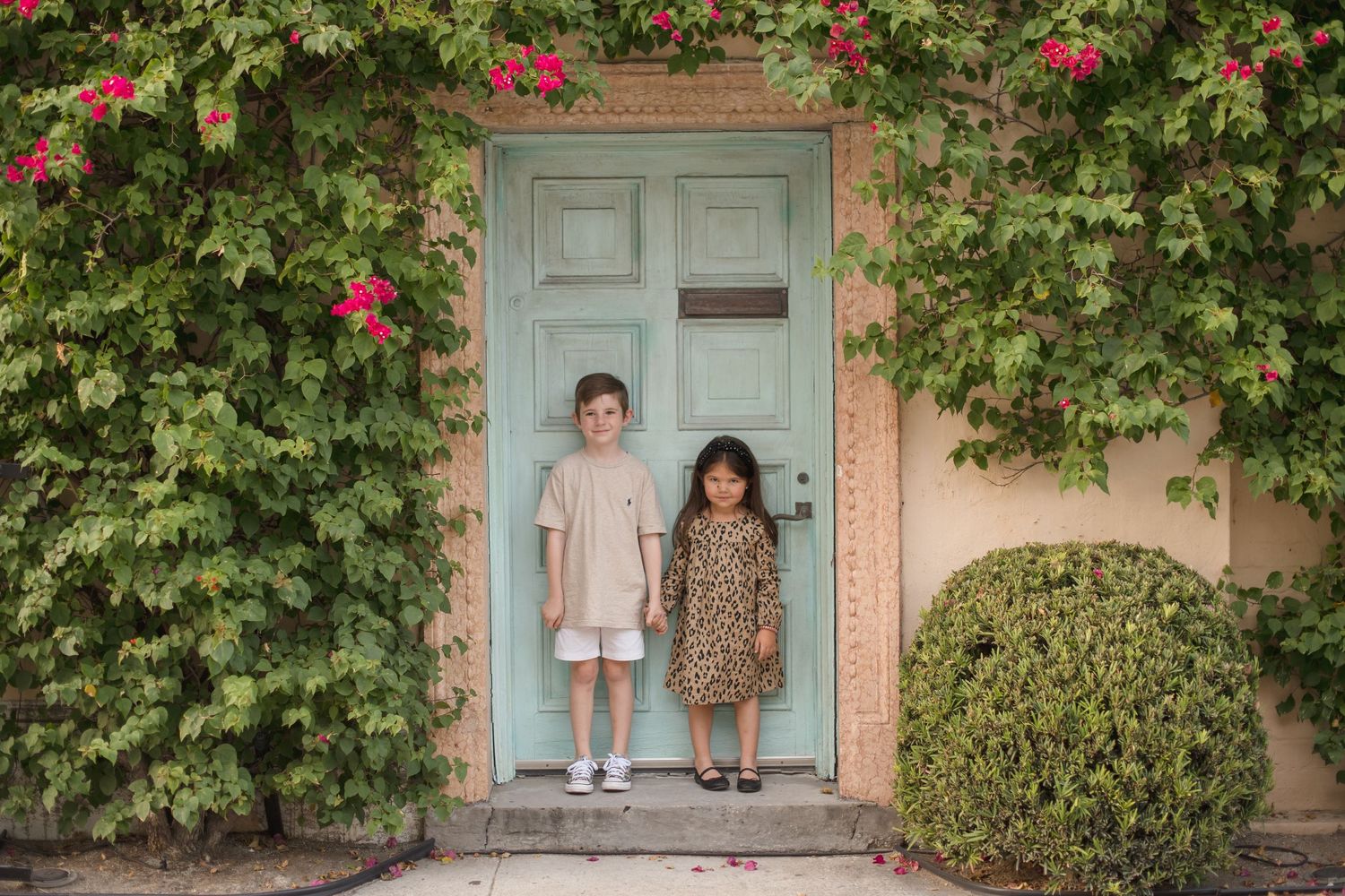 Portrait session against a vintage blue door with pink flowering vines.